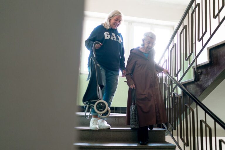 Elderly woman being helped down stairs by a caregiver
