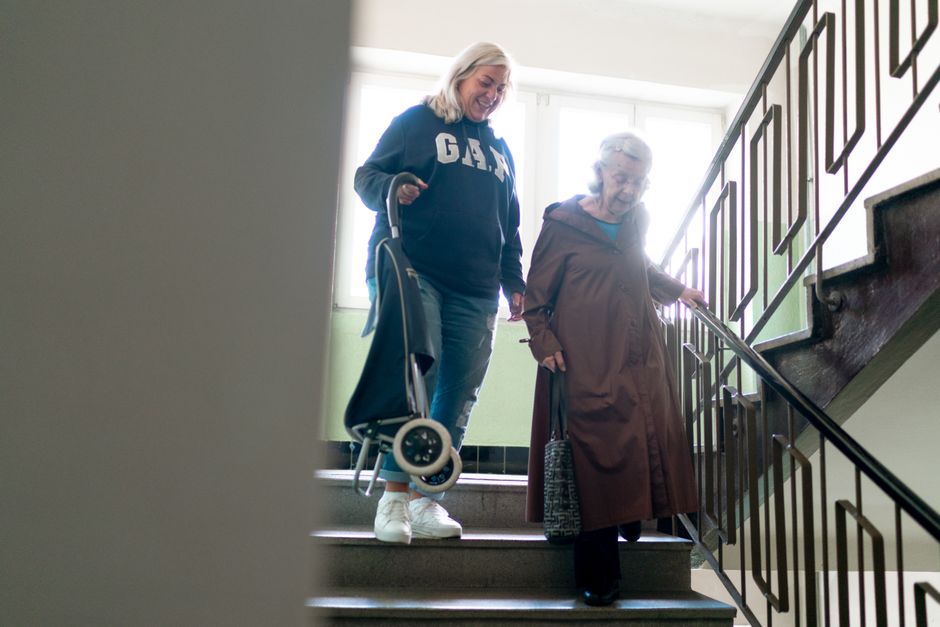 Elderly woman being helped down stairs by a caregiver