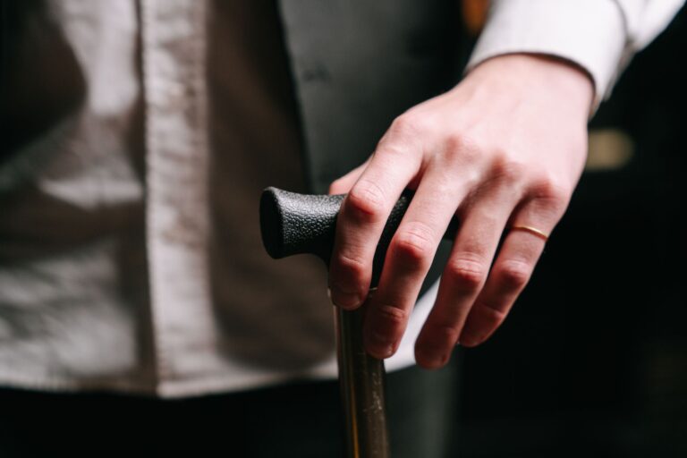 Detailed close-up of a hand wearing a ring, holding a wooden cane, symbolizing support and stability.