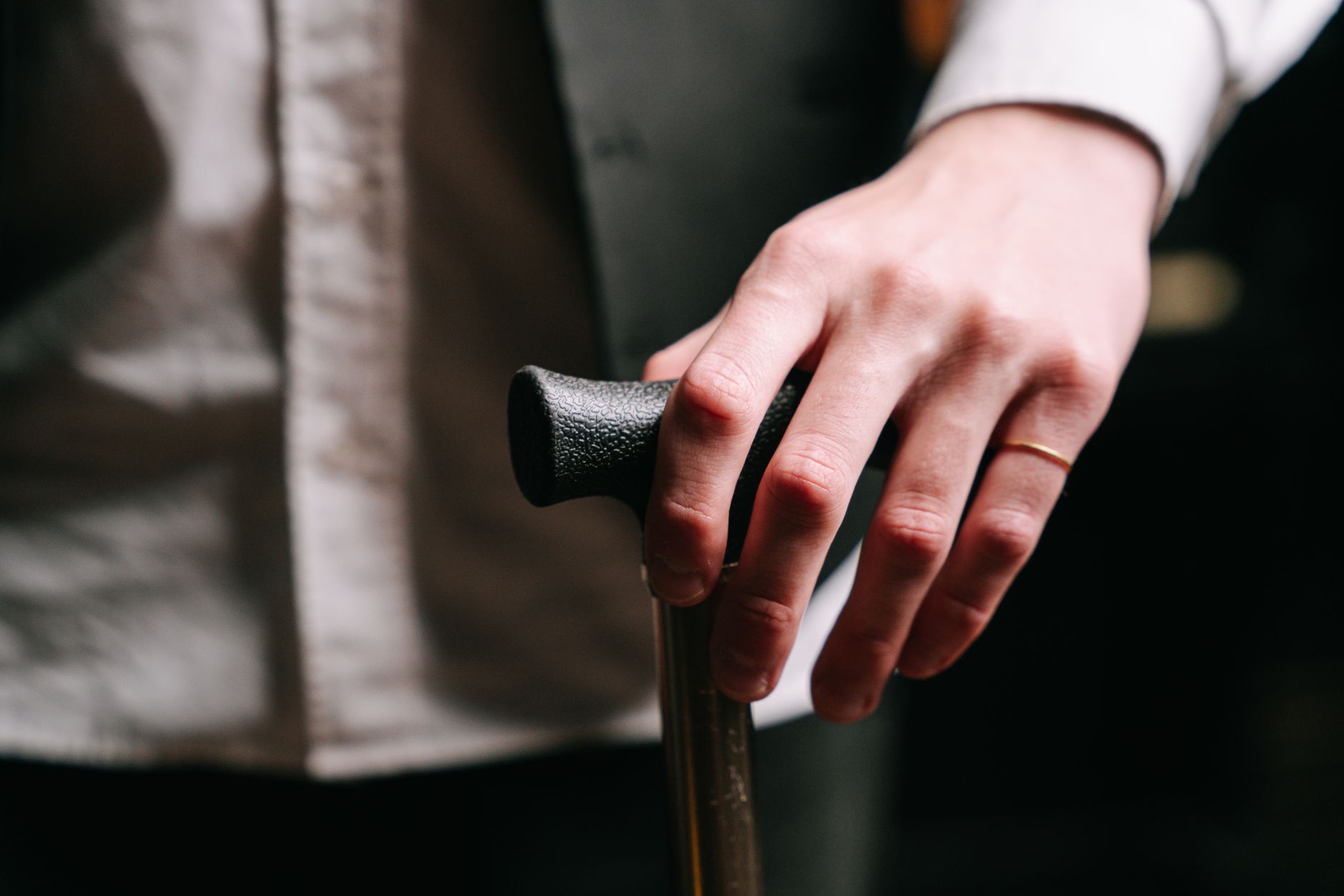 Detailed close-up of a hand wearing a ring, holding a wooden cane, symbolizing support and stability.